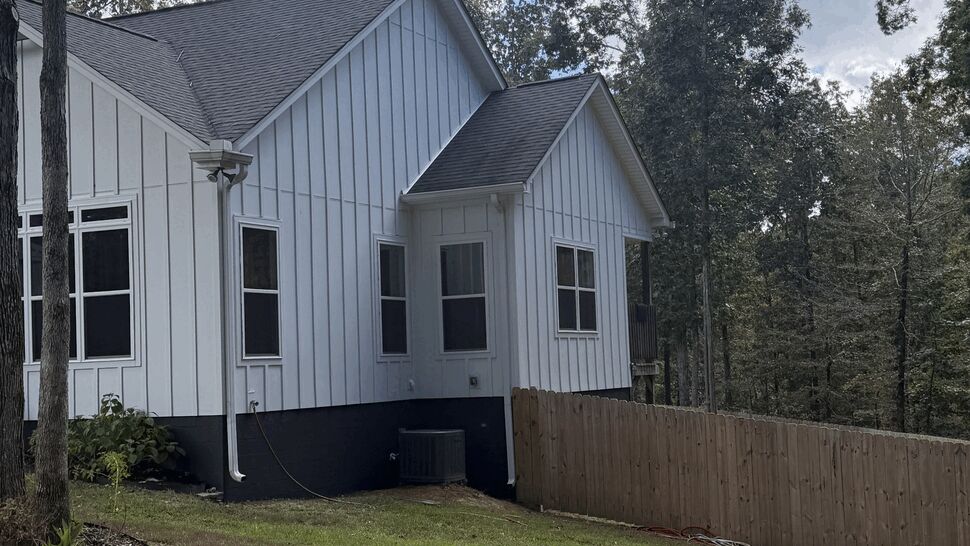 Home Side Siding and Windows | DominionX Side view of a white home with vertical siding, windows, and fenced yard.