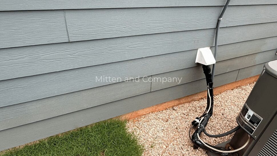 AC unit and siding utility connections | Mitten & Company Outdoor air conditioning unit and utility lines against gray siding on gravel base