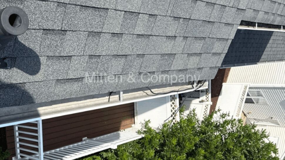 Aerial view of a gray shingled roof and metal gutter over a porch and greenery.
