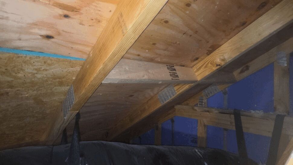 Attic interior showing insulated ductwork, rafters, and plywood sheathing with light staining