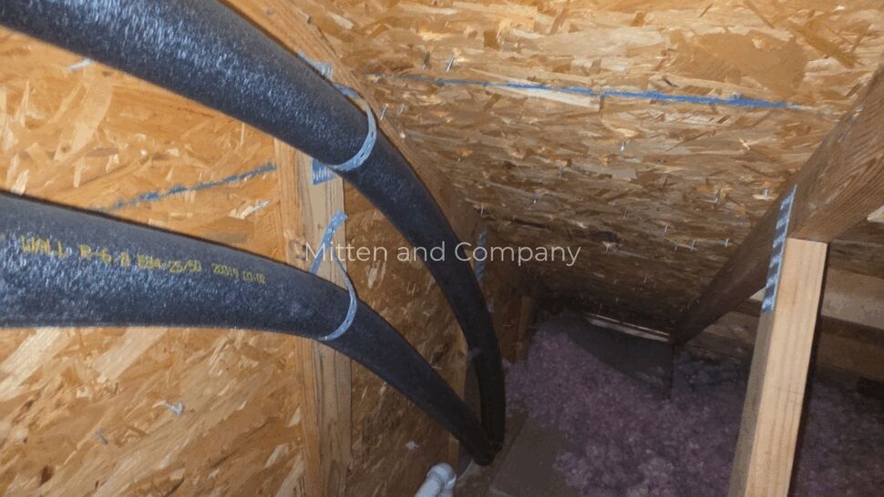 Attic Insulation and Refrigerant Lines | Mitten & Company Attic space showing black insulated refrigerant lines, wood sheathing, and pink insulation