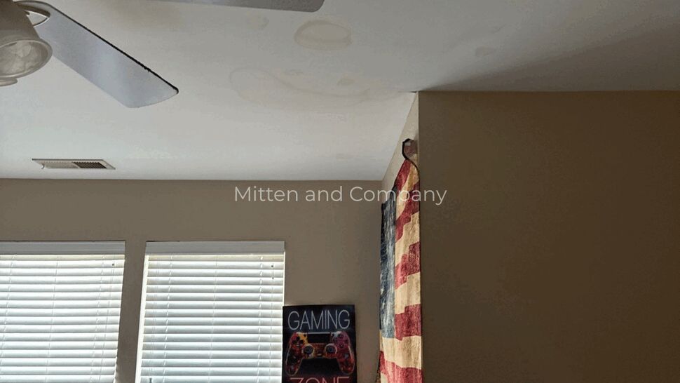 Bedroom Ceiling Water Damage | Mitten & Company Bedroom with ceiling water stains above windows, fan, and an American flag curtain
