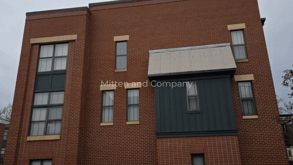 Brick Facade with Metal Awning | Mitten & Company Brick facade with green siding bay and a corrugated metal awning.