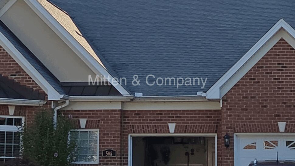 Front view of brick home with gray shingle roof and attached garage.