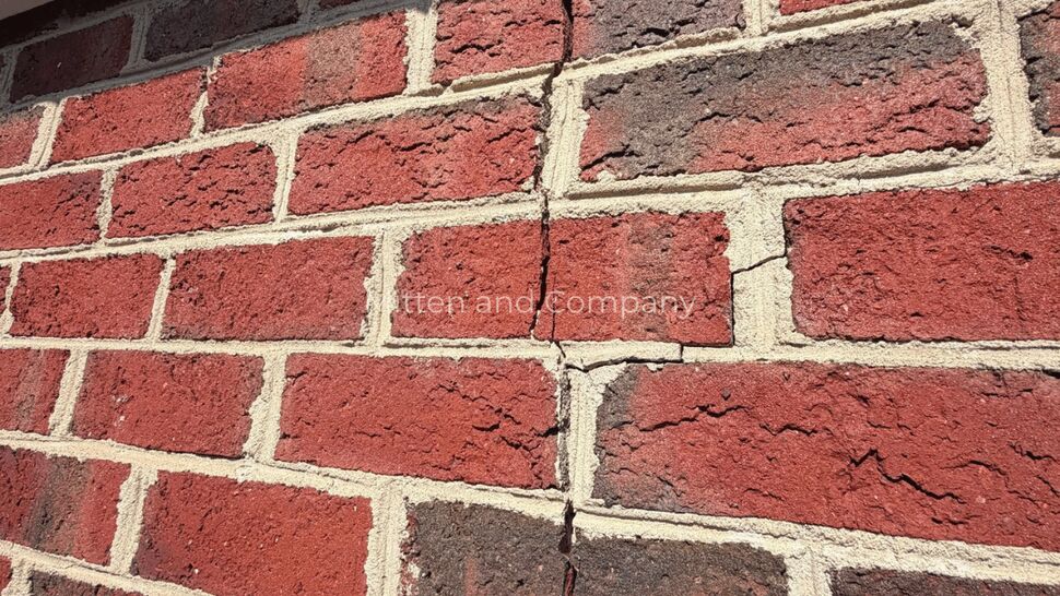 Vertical crack in brick wall | Mitten & Company Close-up of a vertical crack through red brick and mortar on an exterior wall