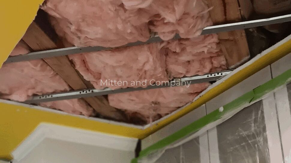 Close-up of a damaged ceiling showing pink insulation and exposed framing.