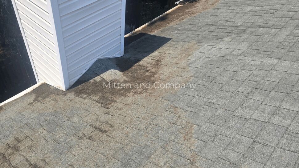 Shingles around a white chimney with dark staining and granule loss