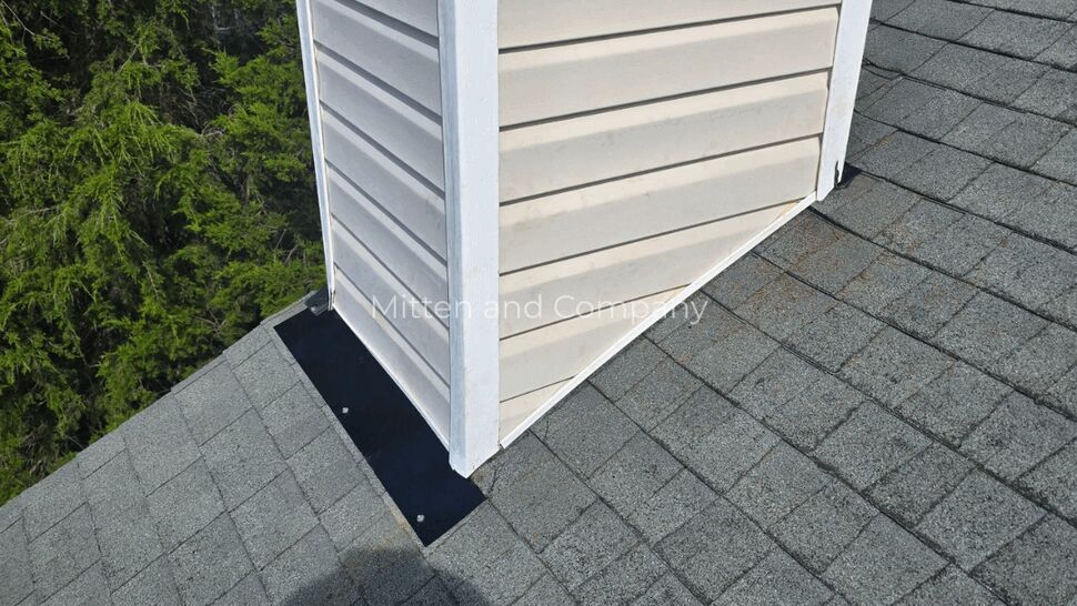 Chimney side with step flashing and asphalt shingles around the base