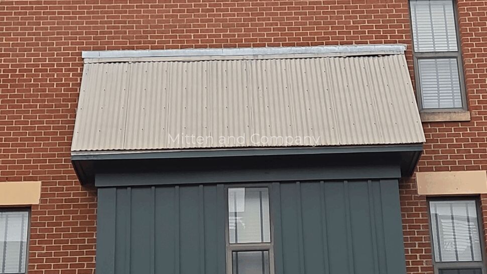 Corrugated Awning and Siding Detail | Mitten & Company Close-up of corrugated metal awning above painted vertical siding on brick wall.