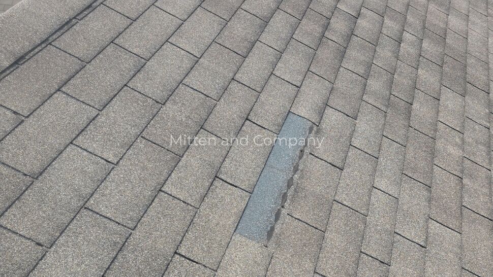 Damaged Roof Shingles | Mitten & Company Close-up of damaged gray roof shingles with exposed areas and a roof vent