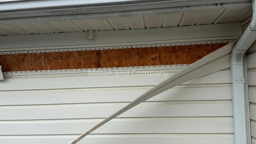 Storm-Damaged Siding and Gutters | Mitten & Company Close-up of damaged siding beneath a shingled roof and gutter system