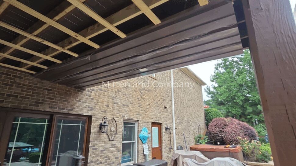 Deck Structure Under Repair | Mitten & Company Exposed deck framing and beams above a brick patio