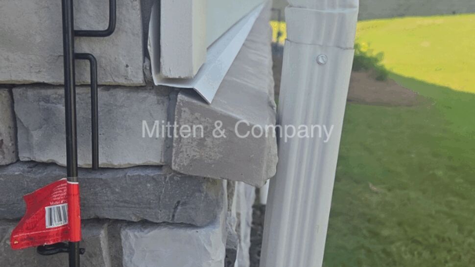 Close-up of downspout elbow and siding flashing on stone corner