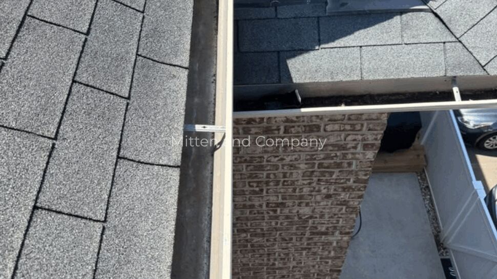 Gable Roof Gutter System | Mitten & Company Gray shingle roof and white gutter system beside a brick gable wall.
