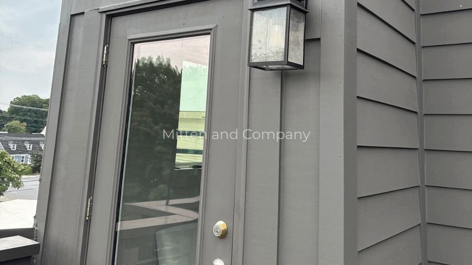Exterior door and siding with lantern | Mitten & Company Gray exterior door with glass panel, adjacent siding, and a wall lantern on a rooftop unit.