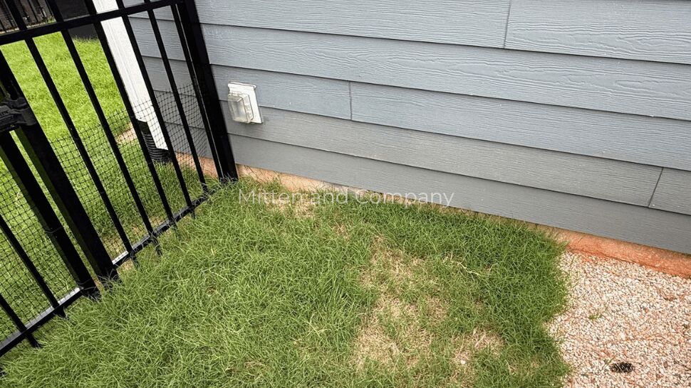 Gray horizontal siding near lawn and fence | Mitten & Company Gray horizontal siding on house exterior with patchy lawn and black metal fence