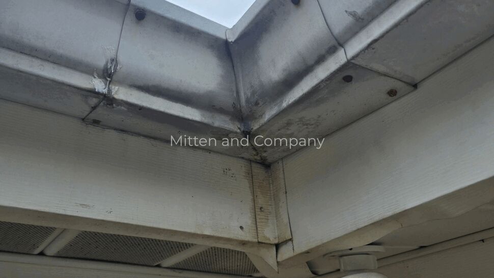 Gutter Corner Inspection | Mitten & Company Close-up of a stained gutter corner beneath a roof overhang