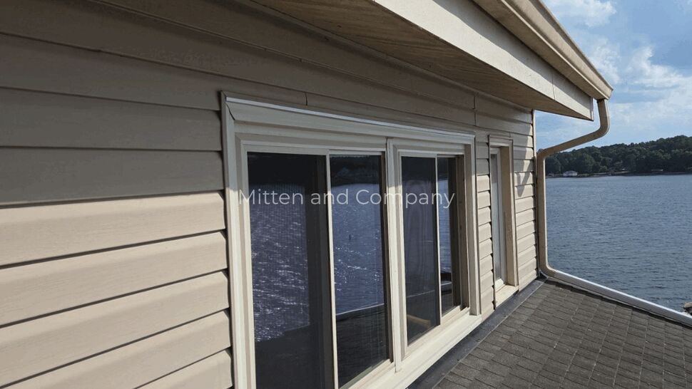 Gutter and downspout at roof edge | Mitten & Company Gutter and downspout along beige siding over shingled roof
