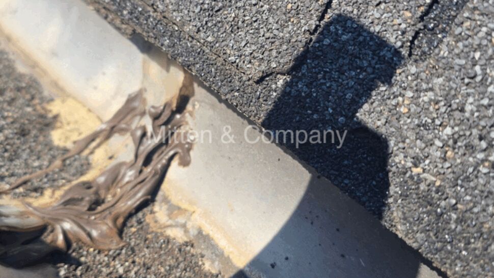 Excess brown sealant pooled inside a metal gutter beneath asphalt shingles.