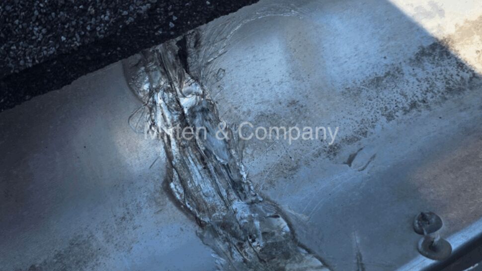 Close-up of a gutter seam with heavy, aged sealant and shingle edge.