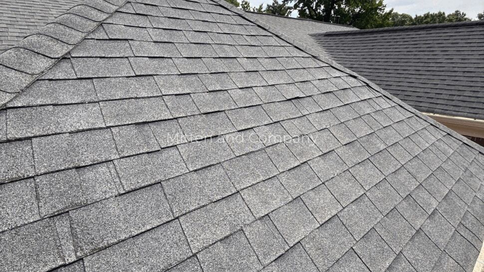 Wide view of a hip roof covered in gray asphalt shingles with trees beyond.