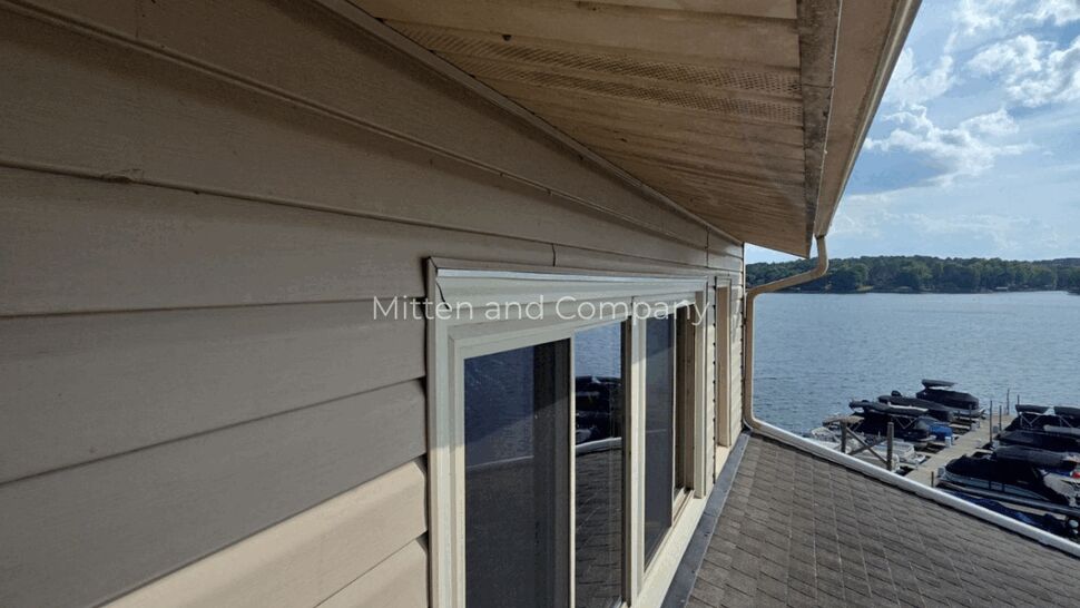 Lakeside siding and window view | Mitten & Company Beige siding and windows above shingled roof with lake view
