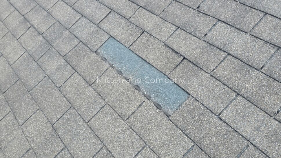 Missing Roof Shingle Section | Mitten & Company Close-up of a gray shingle roof with a missing section exposing the layer below