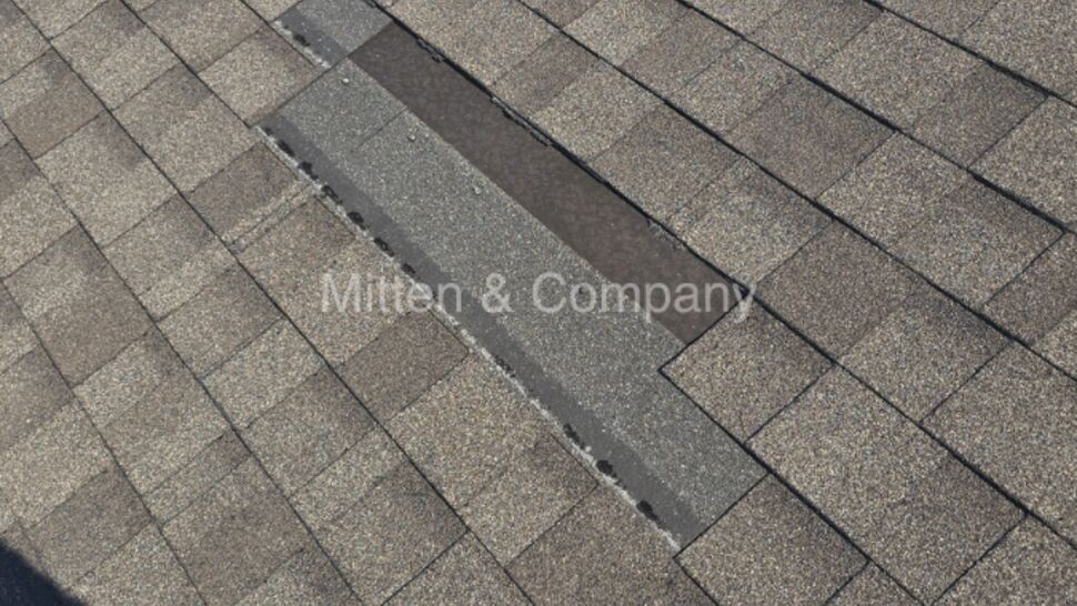 Longitudinal strip of missing shingles exposing underlayment on a roof.