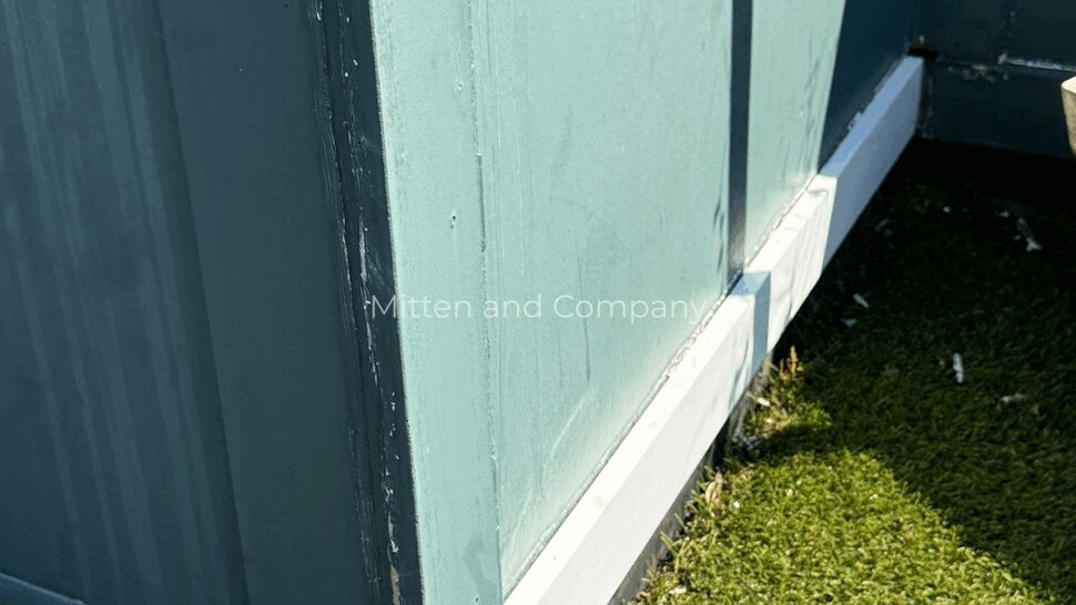 Close-up of parapet base with chipped paint and worn trim next to turf