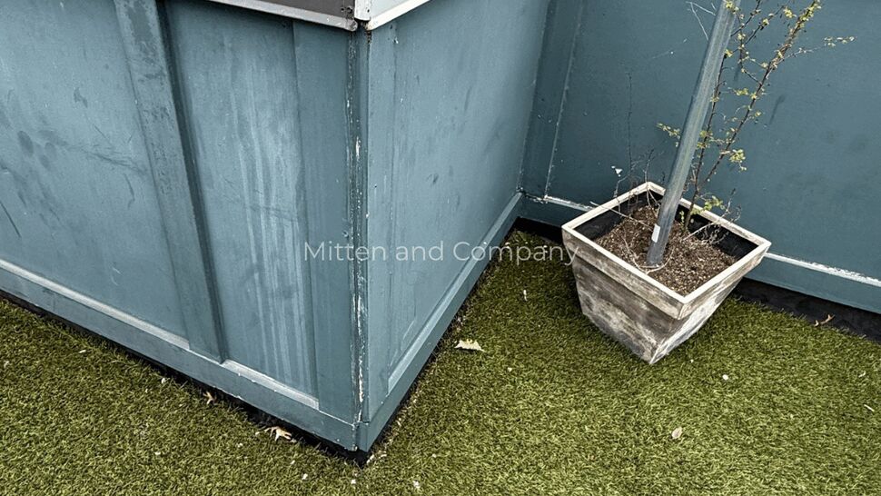 Parapet corner with metal coping | Mitten & Company Corner of rooftop parapet with metal coping, painted siding panels and a planter on artificial turf.