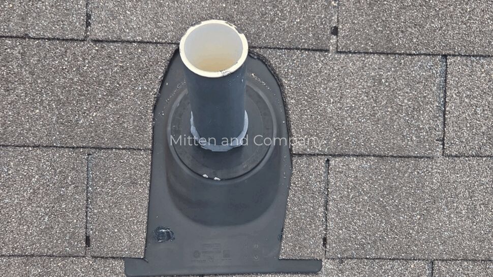 Plumbing vent boot inspection | Mitten & Company Roof plumbing vent boot with surrounding shingles viewed from above
