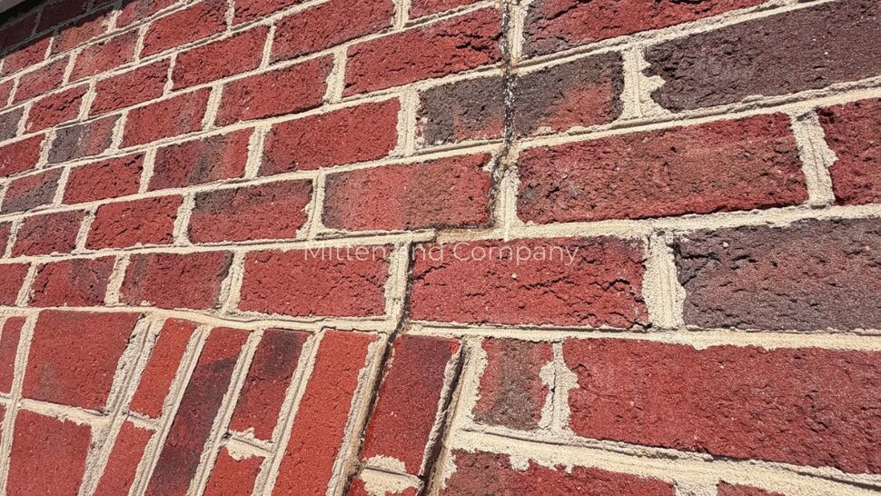 Diagonal mortar crack in brick facade | Mitten & Company Diagonal mortar crack through red brick facade near a header