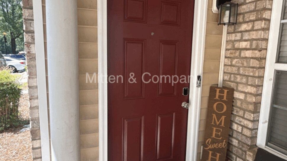 Red exterior front door with brick, tan siding, and porch seating.