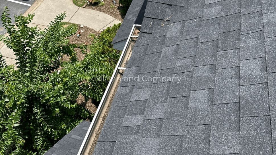 Angled view of asphalt shingles and a debris-filled gutter along roofline