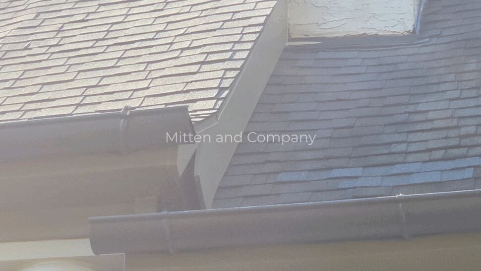 Shingle Wear at Chimney Flashing | Mitten & Company Close-up of chimney base and adjoining shingles showing wear and discoloration.