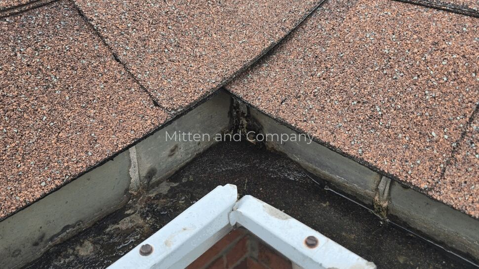 Roof Corner Flashing Inspection | Mitten & Company Roof corner with worn shingles, flashing, and brick chimney visible
