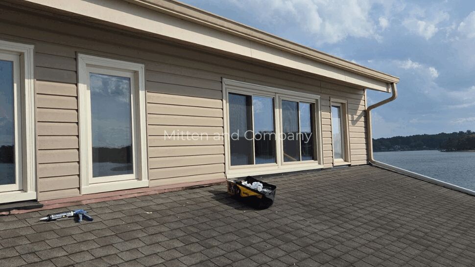 Roofer working on shingled roof near windows | Mitten & Company Shingled roof slope with windows and roofing tools near the edge