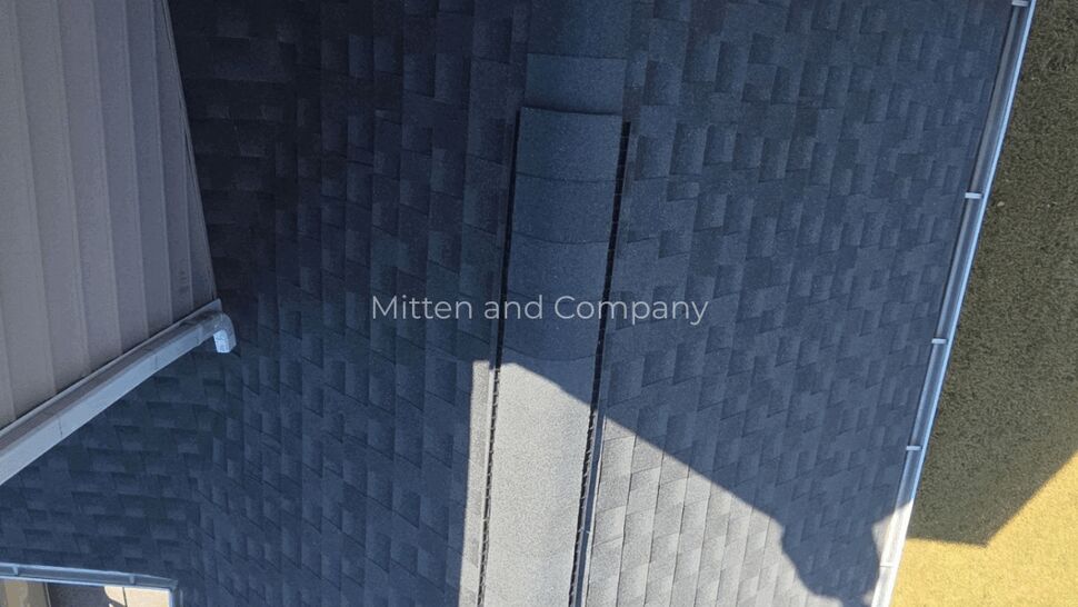 Aerial view of a gray shingle roof, gable, and surrounding lawn.