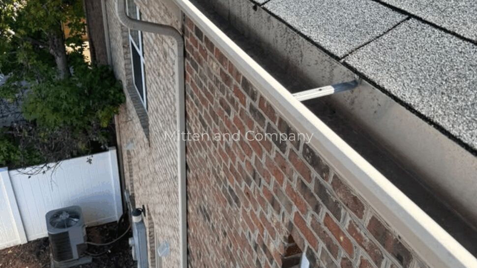 Roof and Gutter Corner | Mitten & Company Close-up of gray shingles and white gutter along a brick home.