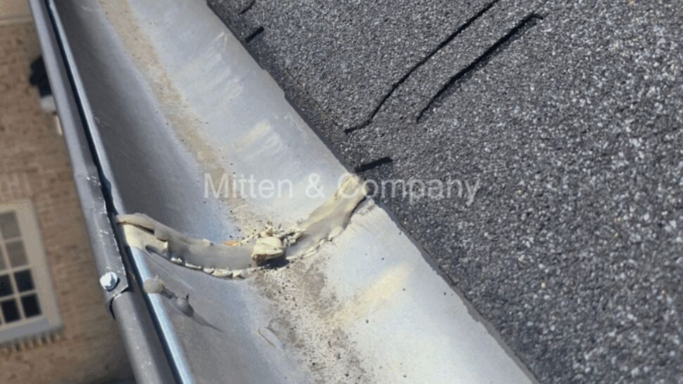 Gutter at the roof edge showing a patched joint and fasteners under shingles.
