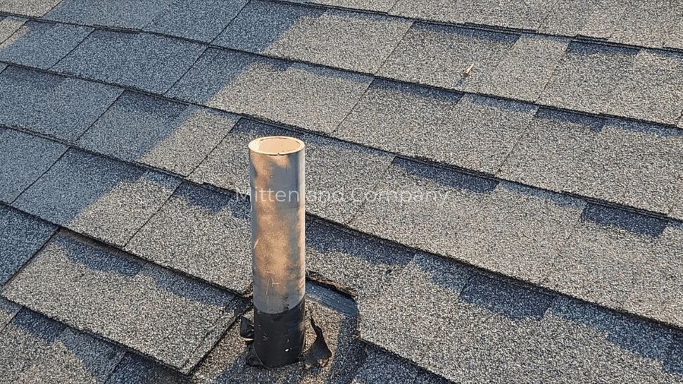Metal roof pipe with black flashing base surrounded by shingles
