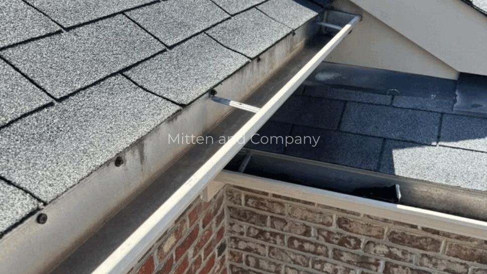Roof Valley Gutter Detail | Mitten & Company Roof valley with gray shingles and white gutters above a brick wall.