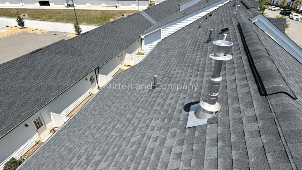Gray multifamily roof with ridge vents and pipe flashing.
