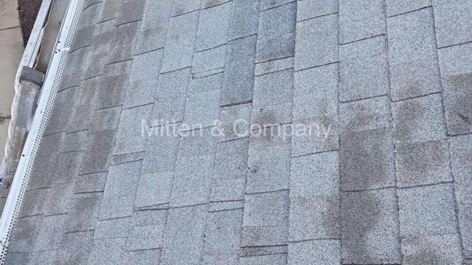 Aerial view of gray asphalt roof with granule loss and dark spots near gutters.