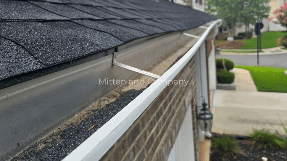 Roof shingles and white gutter running along a brick home