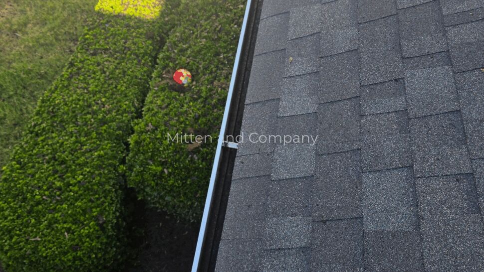 Aerial view of roof edge and clean gutter above green bushes