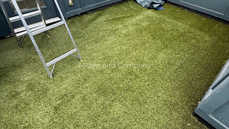 Rooftop turf and ladder | Mitten & Company Rooftop area covered in green artificial turf with a ladder against blue-gray walls.