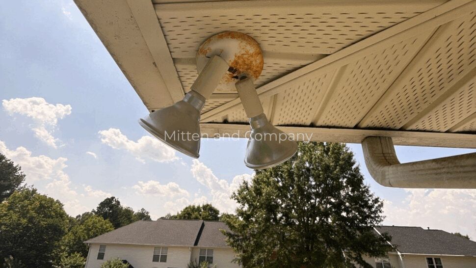 Rusted two-bulb floodlight mounted on soffit above parking area