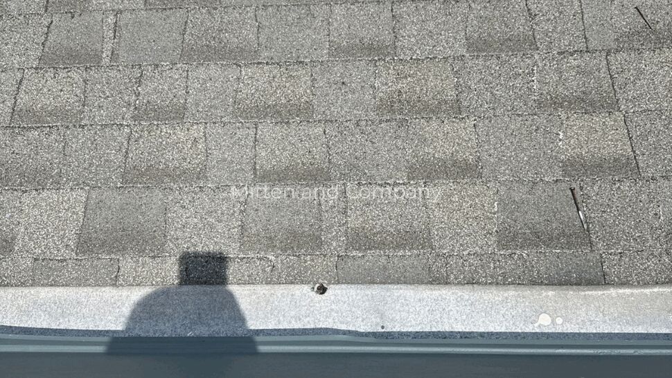 Shingle edge and exposed fastener on parapet | Mitten & Company Close-up of asphalt shingles at a parapet edge with an exposed fastener.