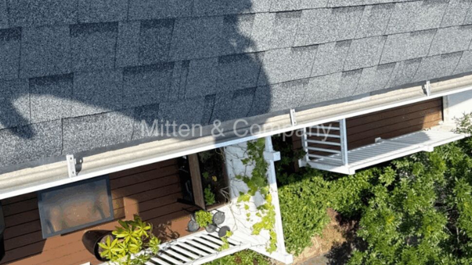 Overhead image of shingled roof casting shadow over a deck and walkway below.